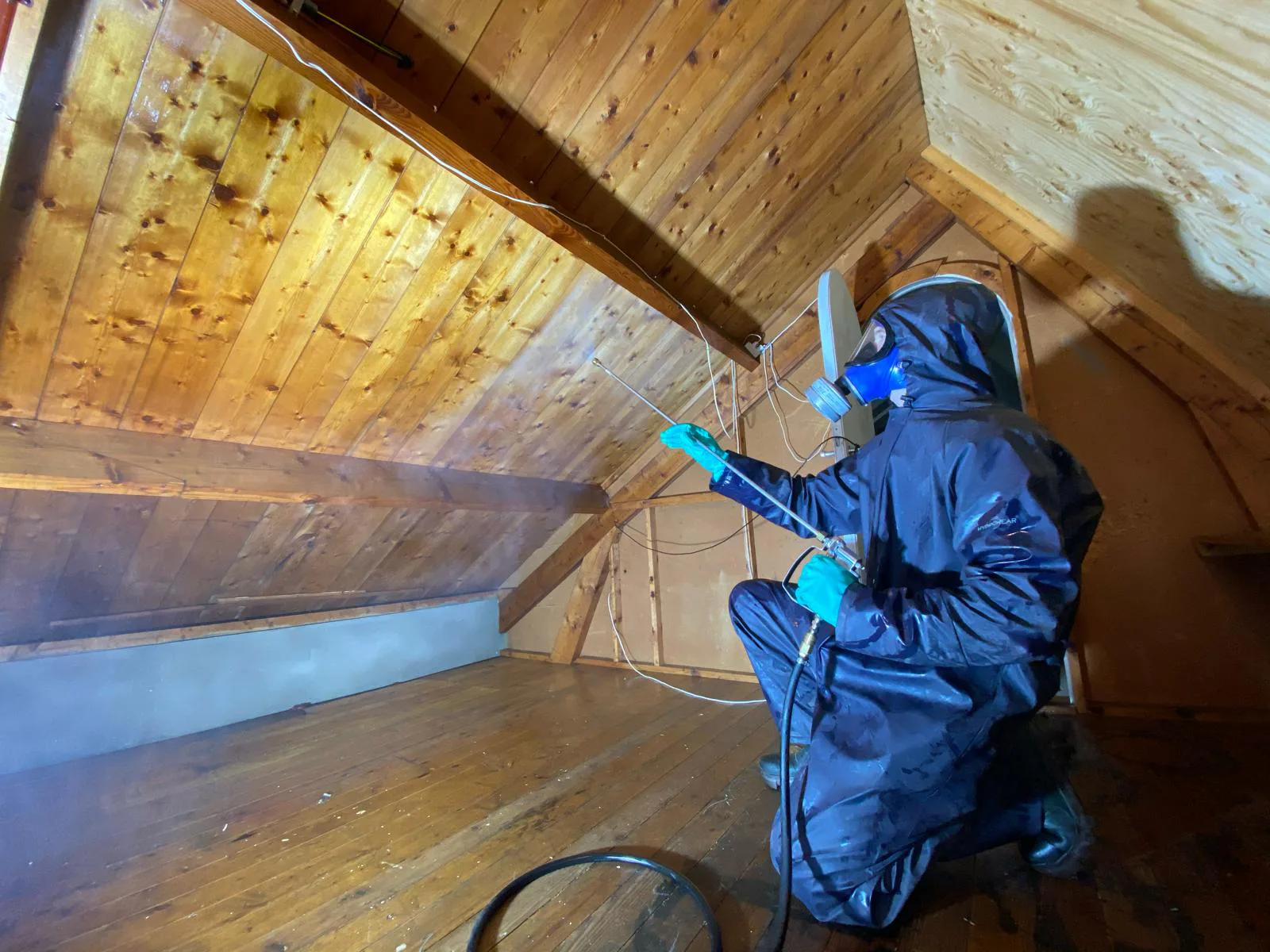 Specialist in beschermende kleding behandelt houten dakbeschot en balken op een zolder