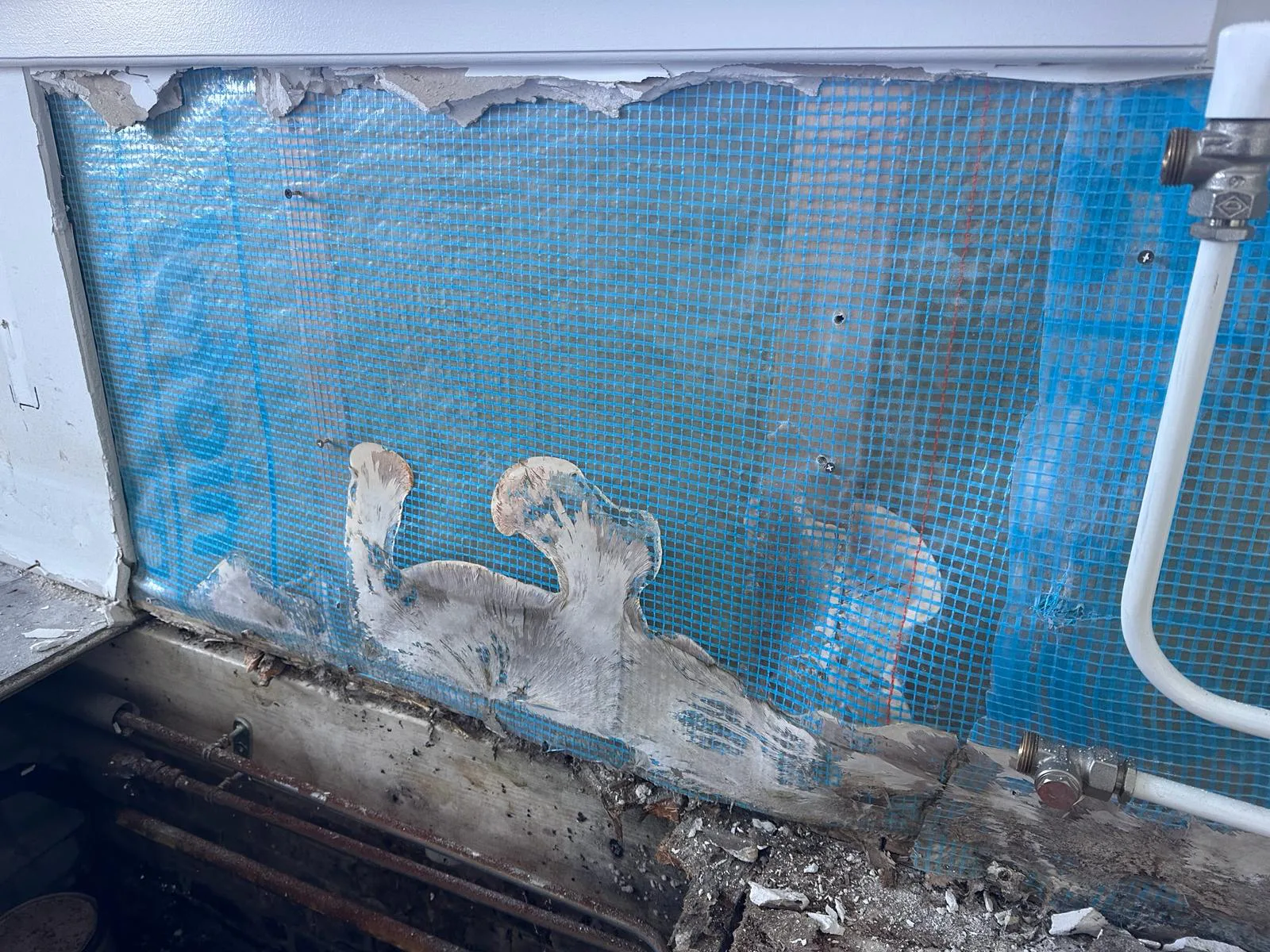 Opengelegde wand achter leidingen met witte groei langs de vloer